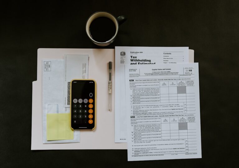 A person organizing paystubs, receipts, and bank statements at a kitchen table with a calculator and cup of coffee.