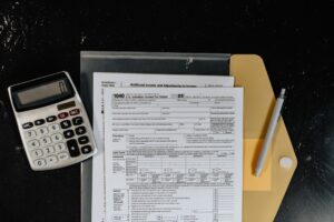 A kitchen table covered in tax forms, receipts, and a laptop, with a person reviewing documents.