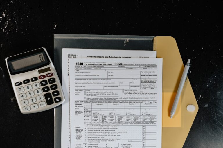 A kitchen table covered in tax forms, receipts, and a laptop, with a person reviewing documents.