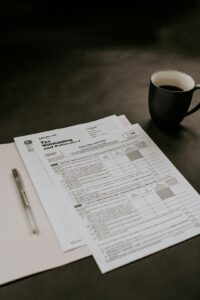 Person reviewing tax forms and receipts at a kitchen table beside a calculator and laptop.