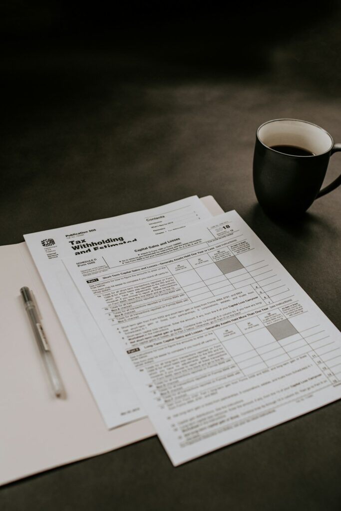 Person reviewing tax forms and receipts at a kitchen table beside a calculator and laptop.