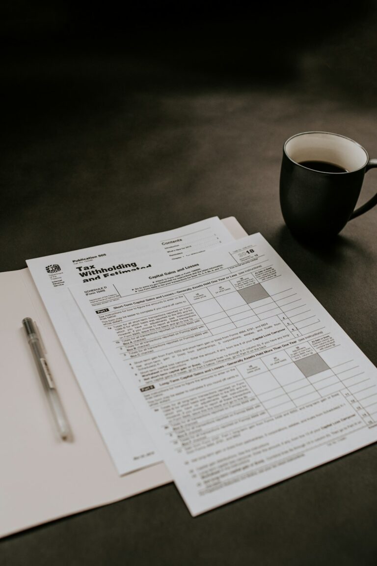 Person reviewing tax forms and receipts at a kitchen table beside a calculator and laptop.