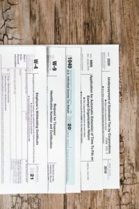 A person sitting at a kitchen table sorting tax documents and forms with a laptop open.